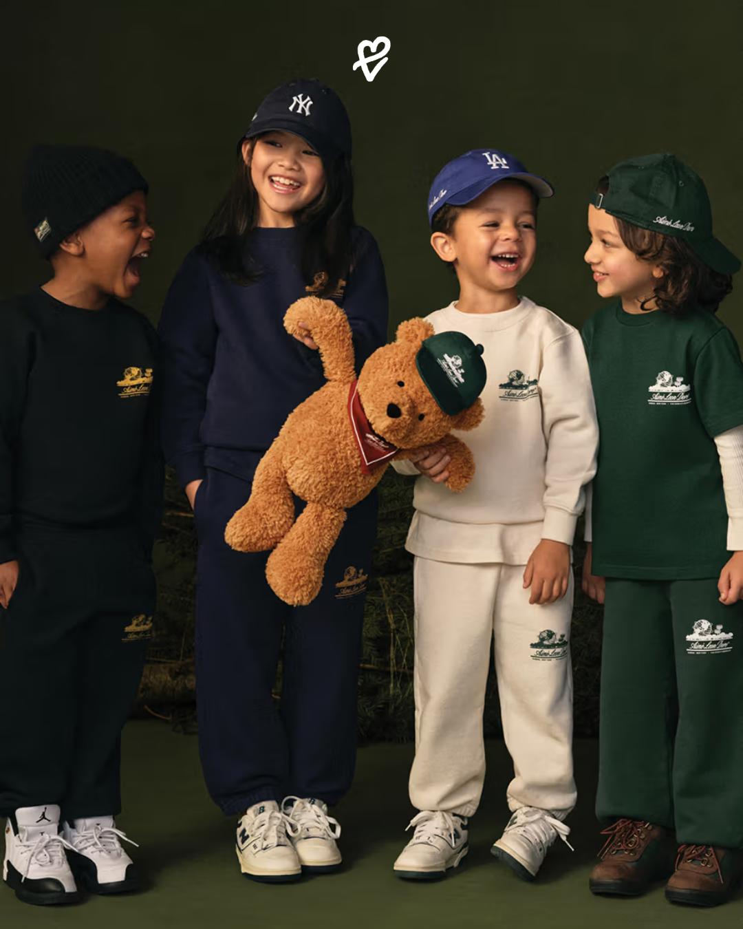 Aimé Leon Dore FW25 Holiday koleksiyonundan hokey forması giymiş bir model ve Buddy Bear pelüş oyuncakla dekore edilmiş bir masa başı sahnesi