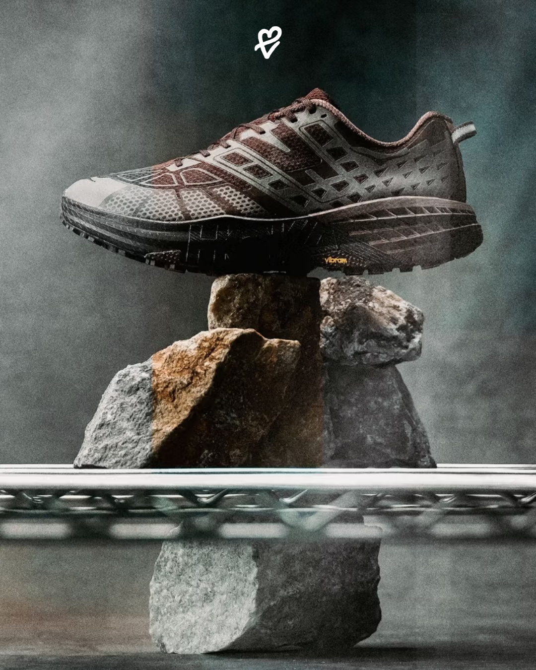 Hoka Stealth / Tech koleksiyonuna ait Walnut ve Cast Iron renkli Mafate Speed 2 ile Speedgoat 2 modelleri, şehir fonunda minimalist bir kompozisyonla sergileniyor.