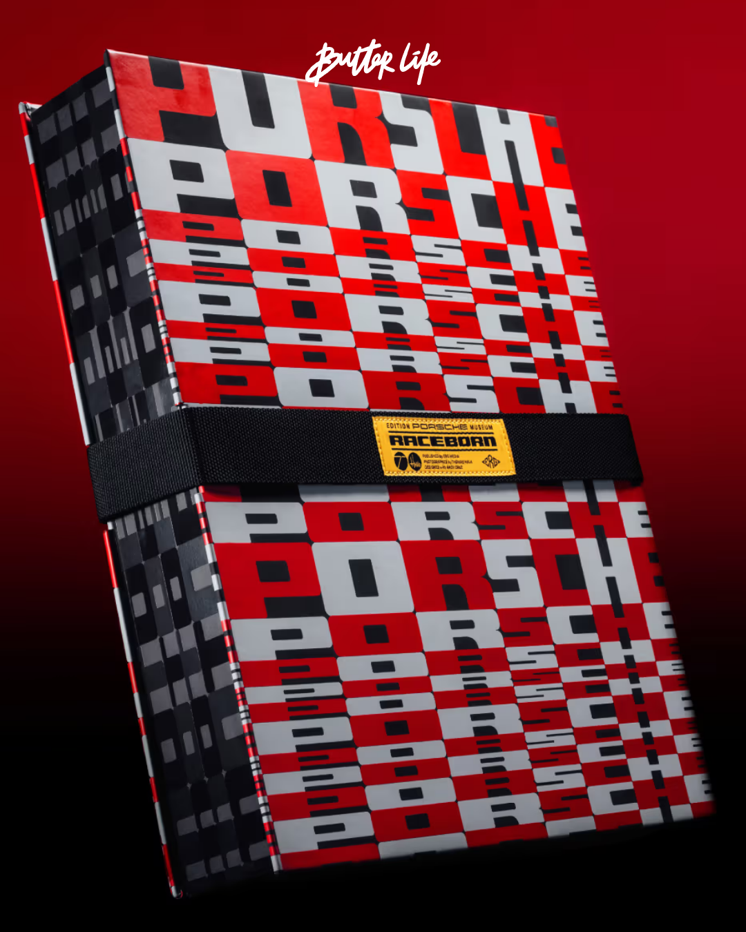Artifacts: Porsche Motorsport kitabının kırmızı kapak tasarımı ve motor sporlarına özgü kemer tokası detayının öne çıktığı ön yüz görseli.