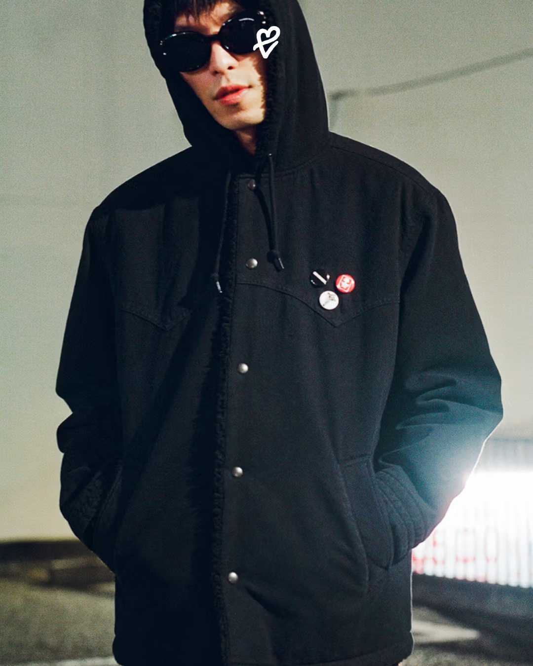 Supreme ve Number (N)ine Fall 2025 koleksiyonundan, Schott® Perfecto ceketli ve suni kürklü kapüşonlu üst giymiş modelin siyah-beyaz lookbook fotoğrafı.