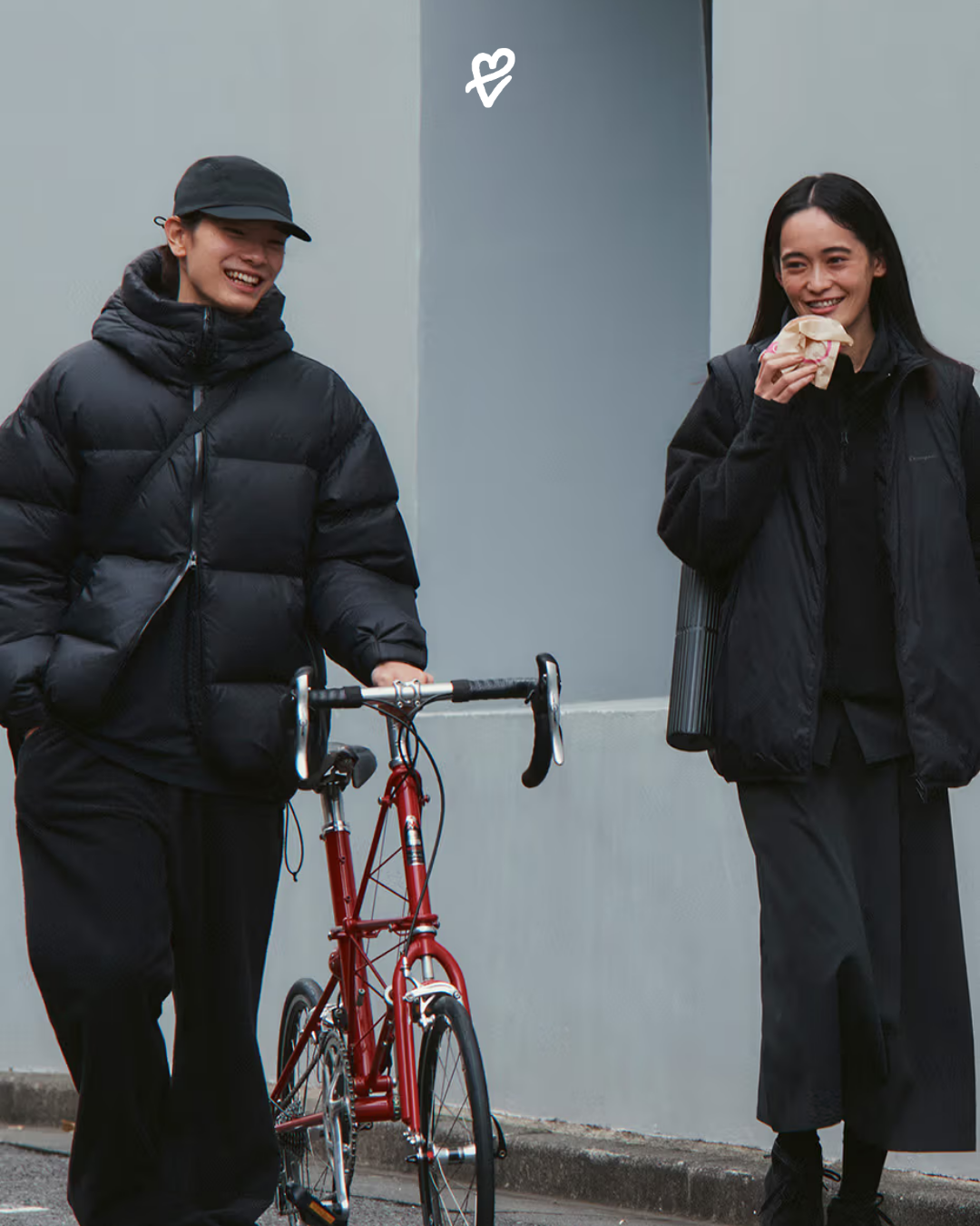 Champion Black Edition FW25 koleksiyonundan siyah mont giymiş bir model, mimari şehir arka planında yürürken.